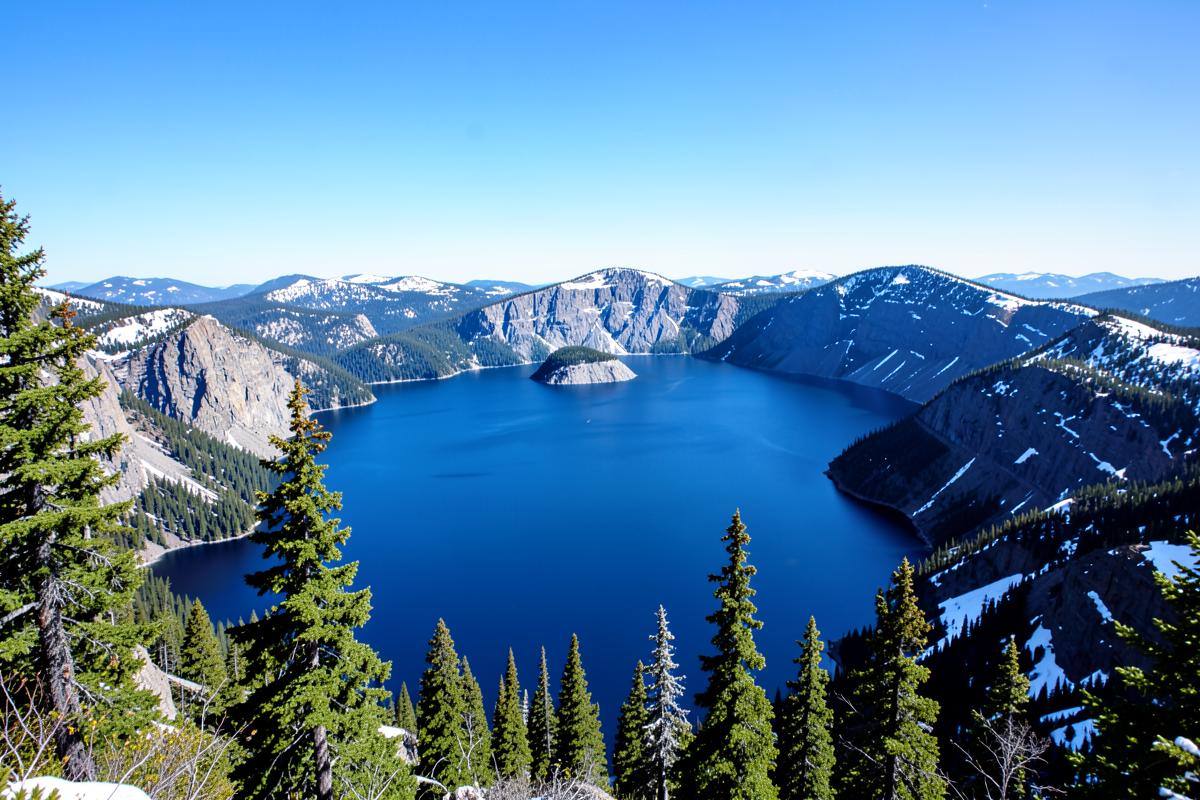 Tiefblauer Kratersee des Crater Lake mit Wizard Island und schneebedecktem Kraterrand